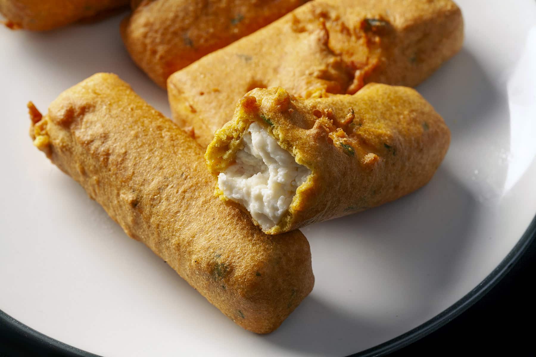 A plate of paneer pakora, with one bitten in half.