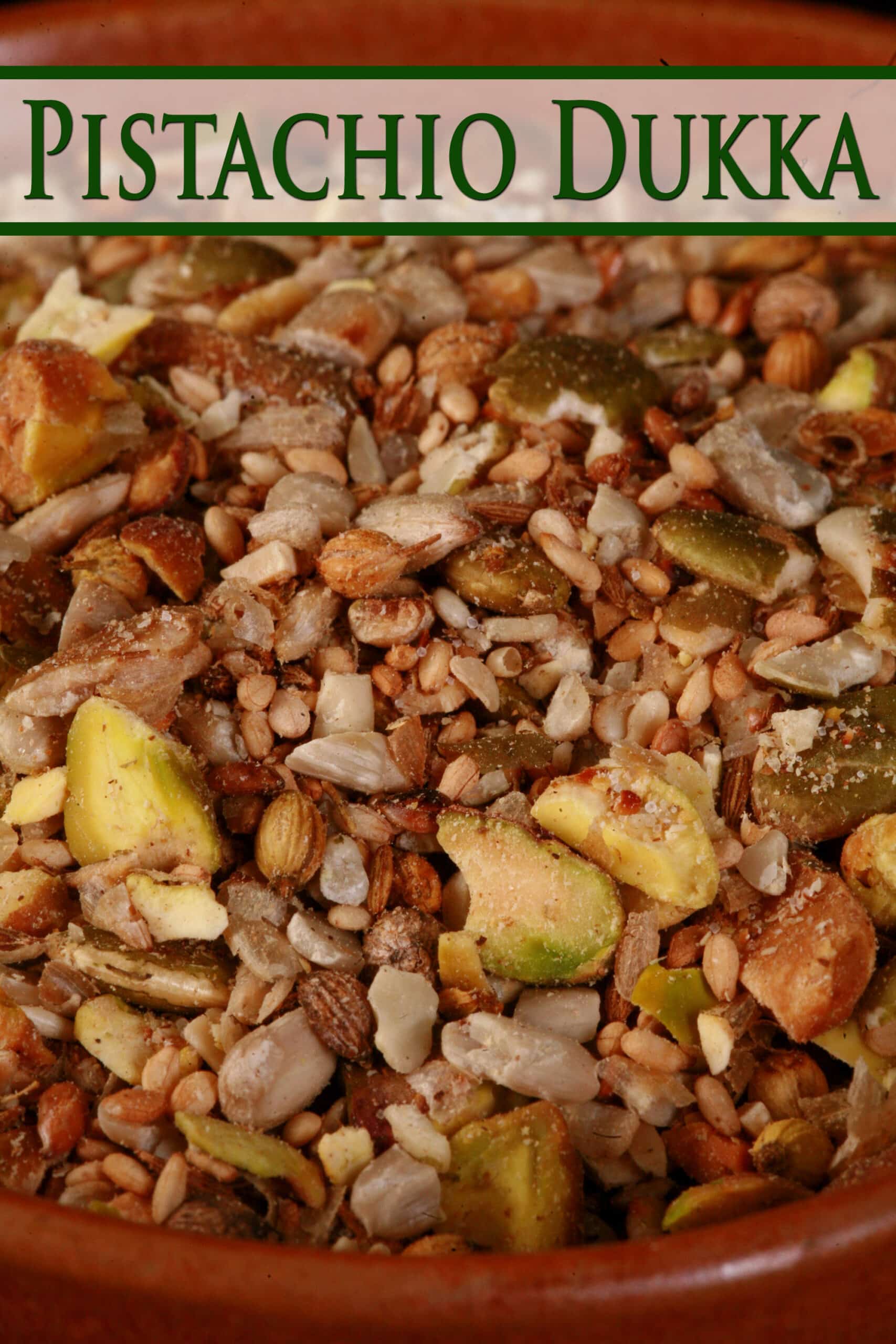 A small brown bowl of pistachio dukkah spice mix. Chunks of pistachios, coriander, sunflower seeds, and pumpkin seeds are visible.