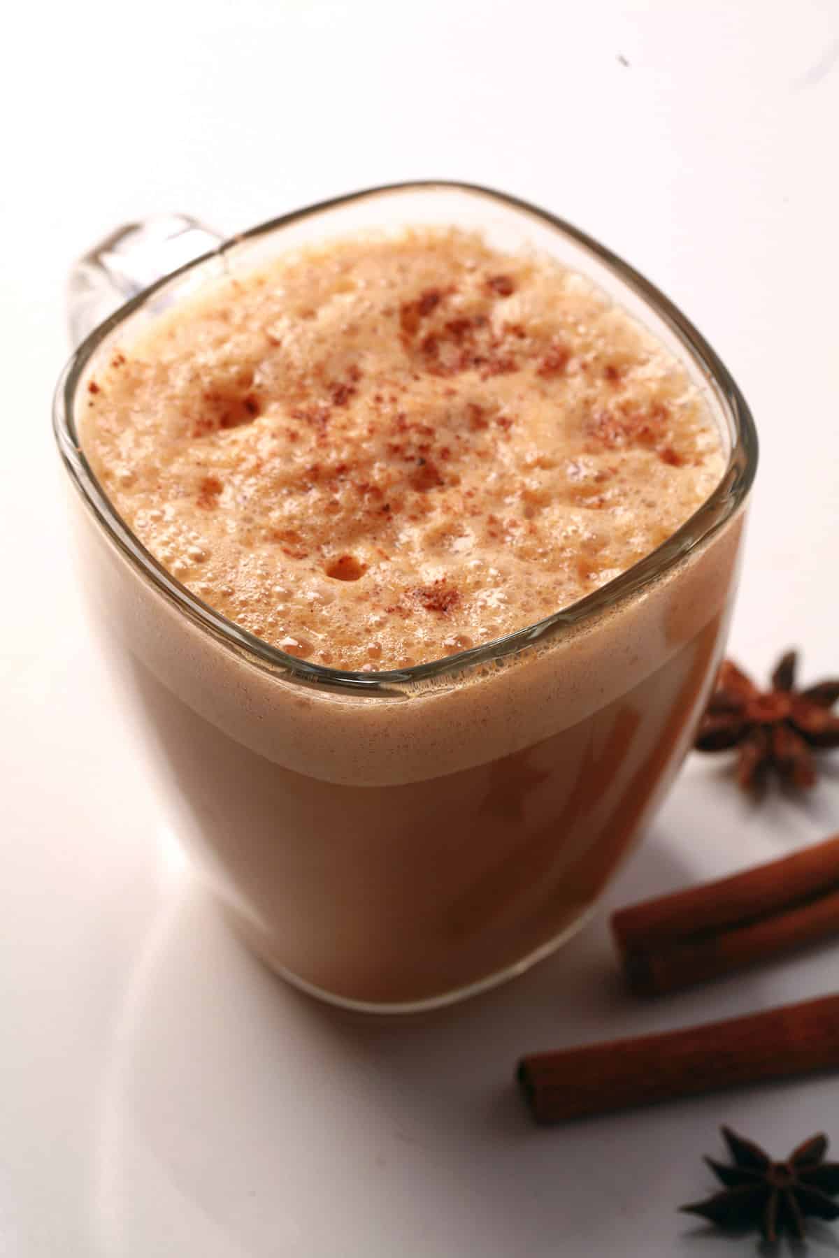 A glass mug of pumpkin chai latte, with cinnamon sticks and star anise next to it.