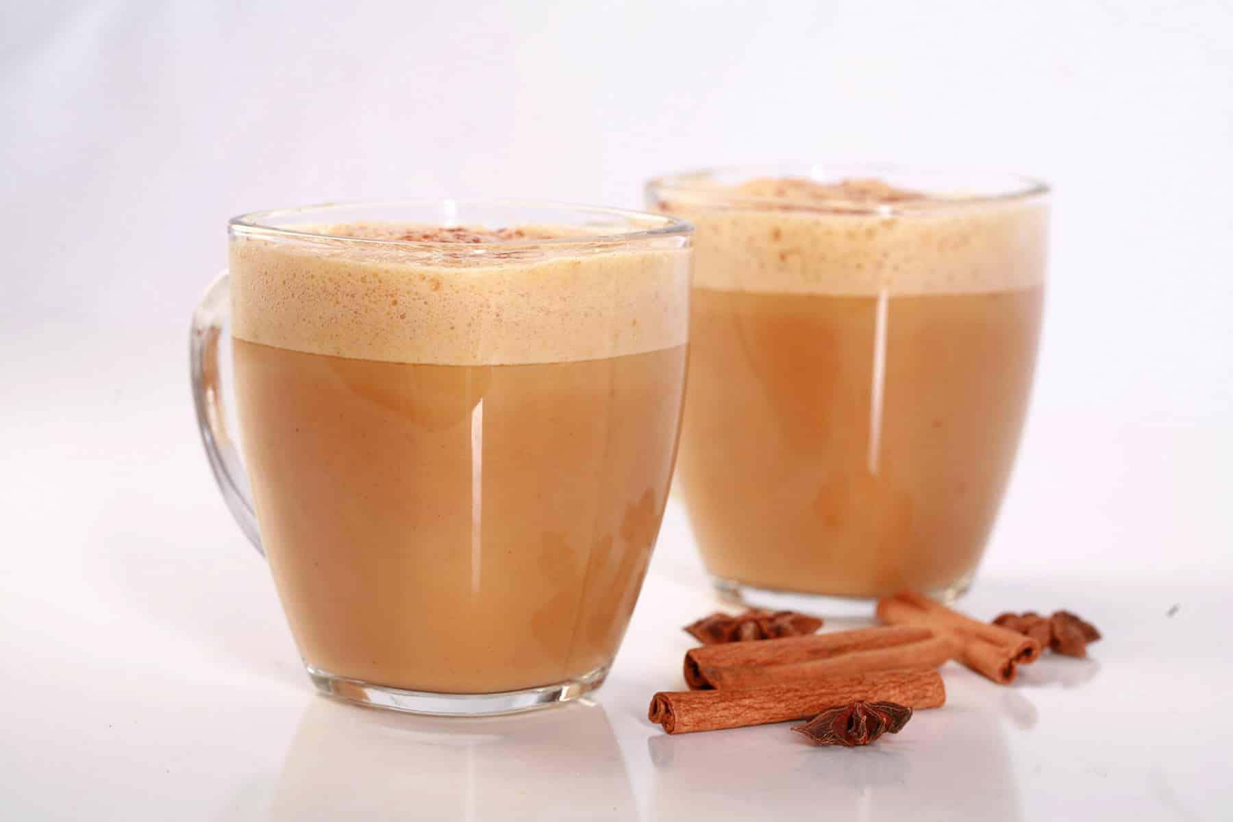 2 Pumpkin Chai Lattes in glass mugs, with cinnamon sticks and star anise around them.