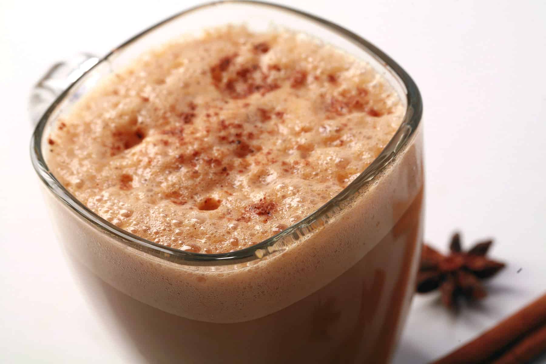A glass mug of pumpkin chai latte, with cinnamon sticks and star anise next to it.