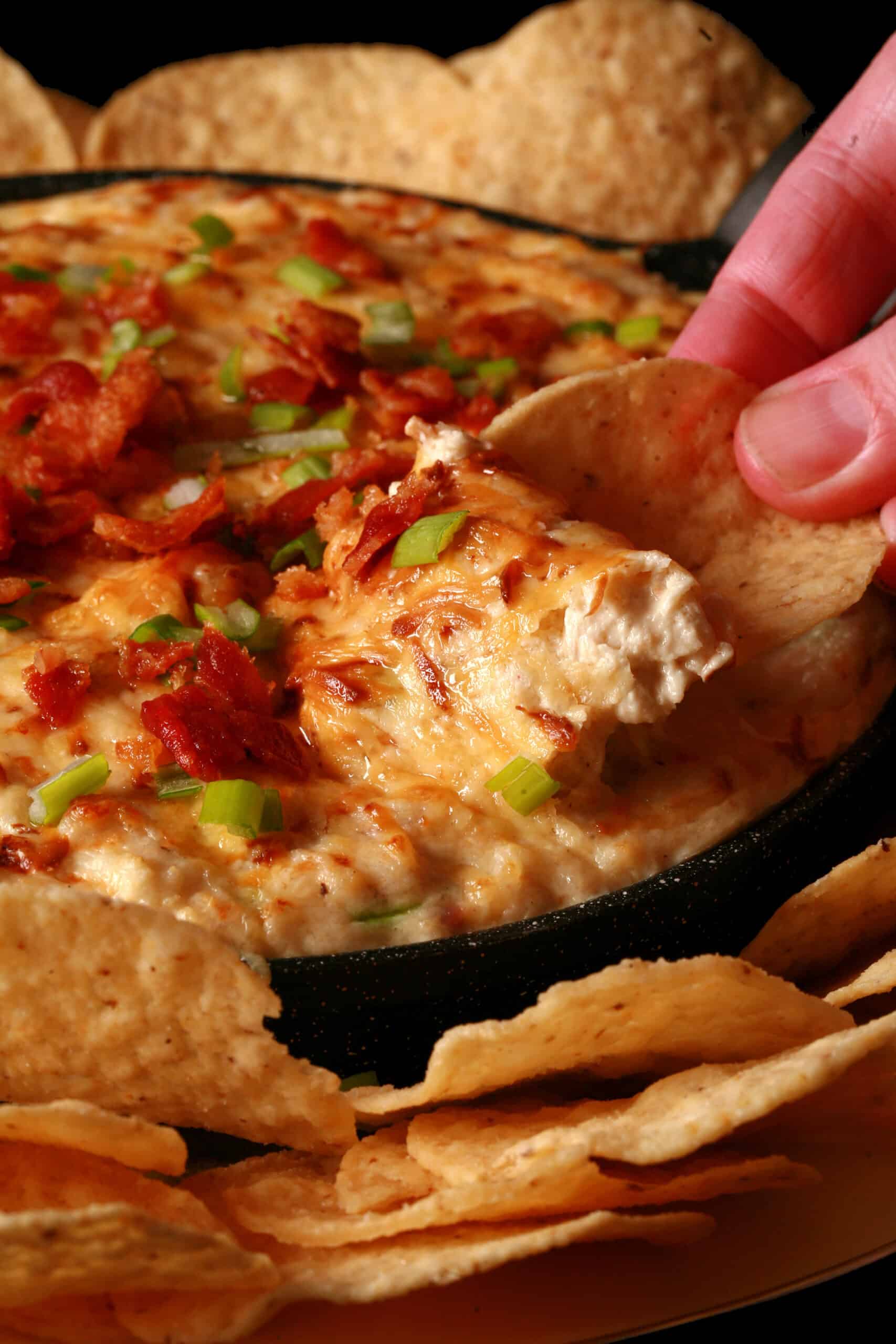 A tortilla chip being dipped into a pan of smoky hot crab dip.