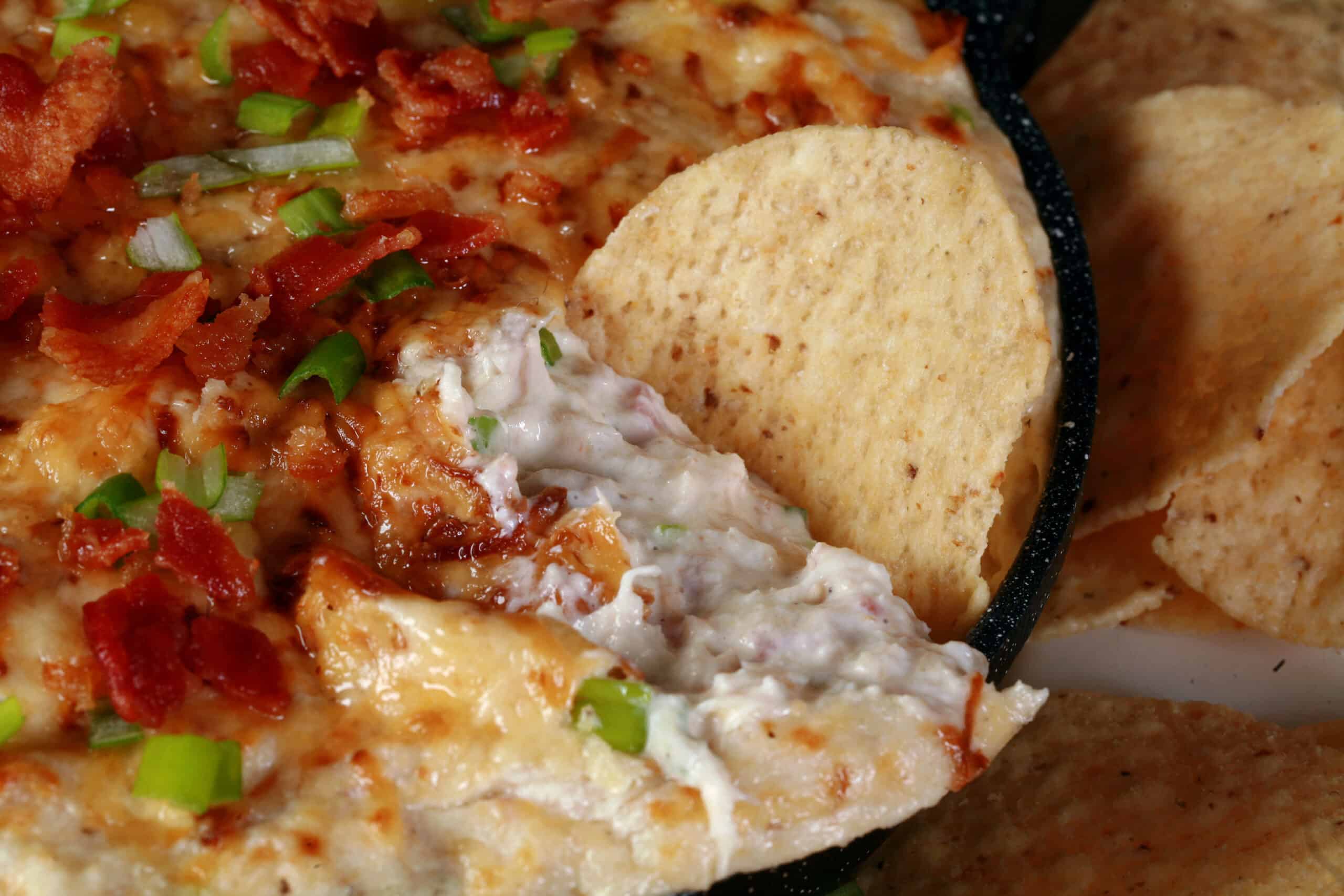 A tortilla chip being dipped into a pan of smoky hot crab dip.