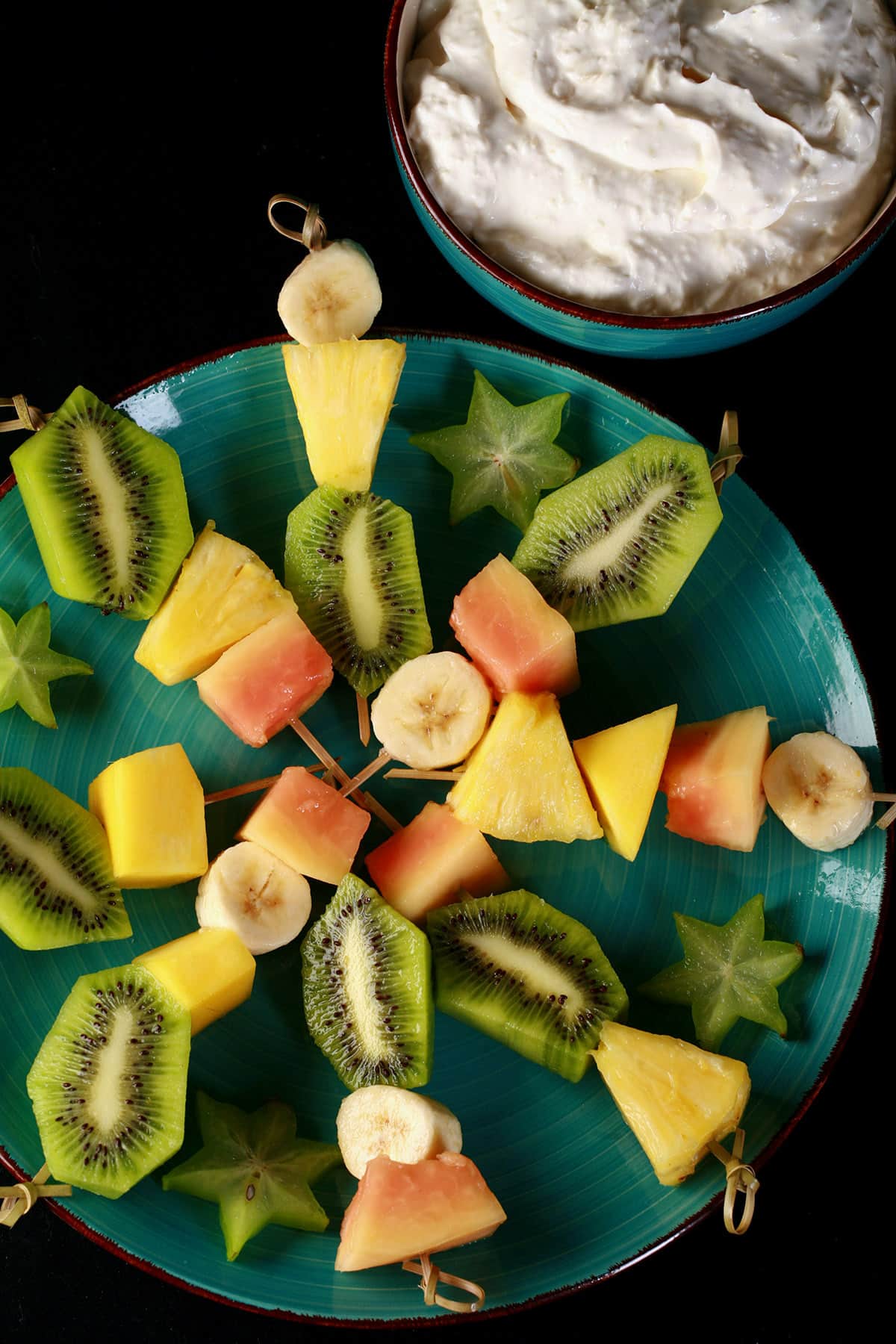 A plate of mixed fruit tropical skewers and a bowl of pina colada dip.