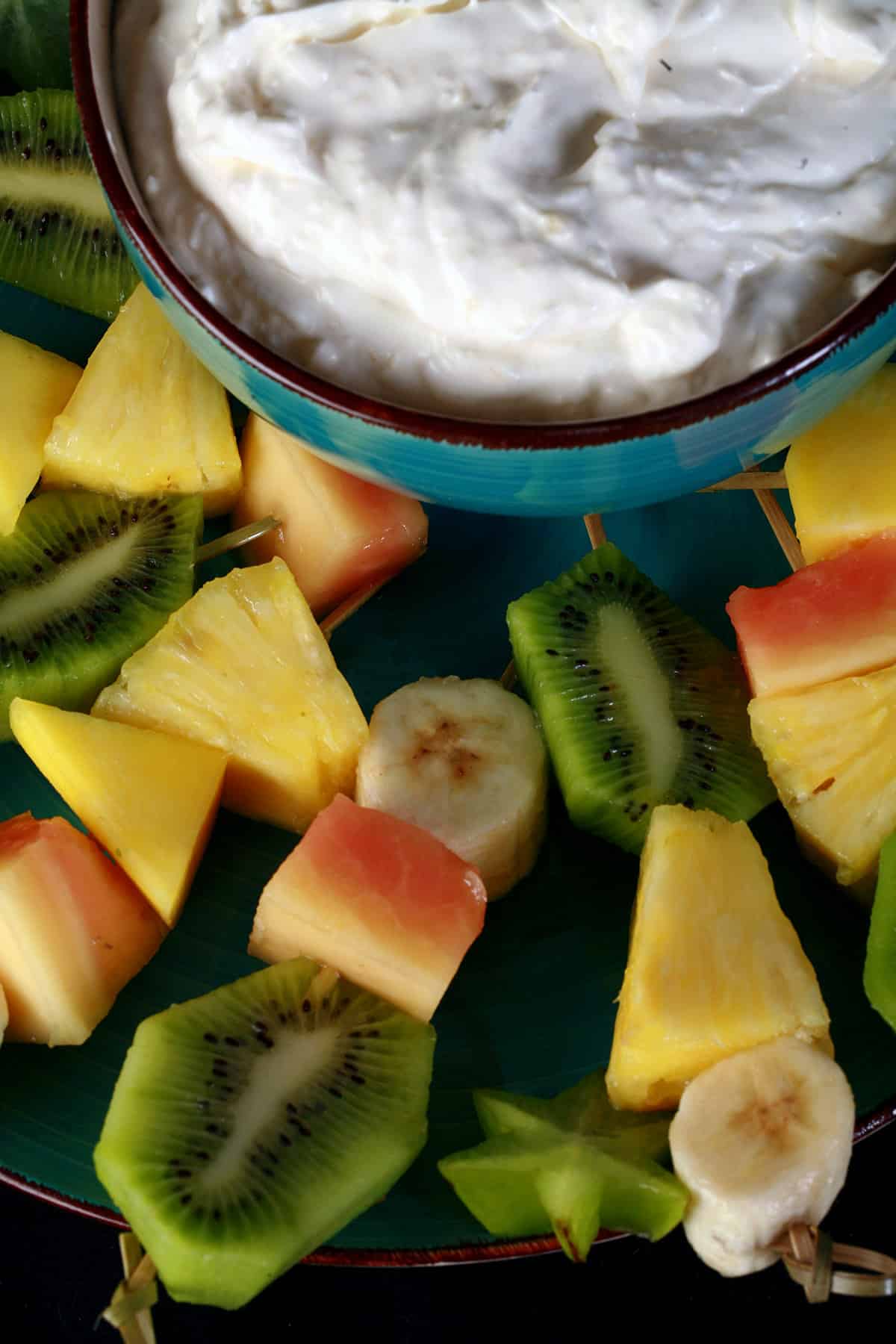 A plate of tropical fruit skewers and a bowl of pina colada cheesecake dip.