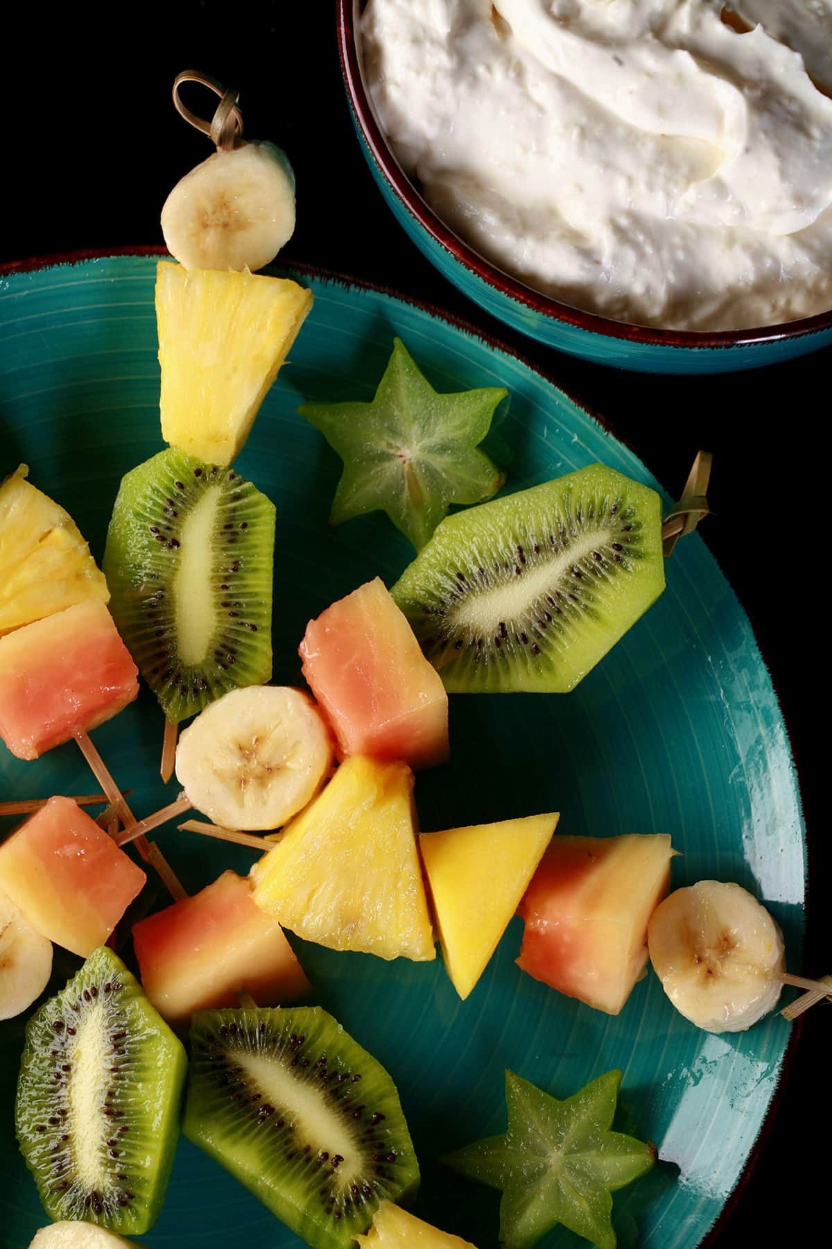 A plate of tropical fruit skewers and a bowl of pina colada cheesecake dip.