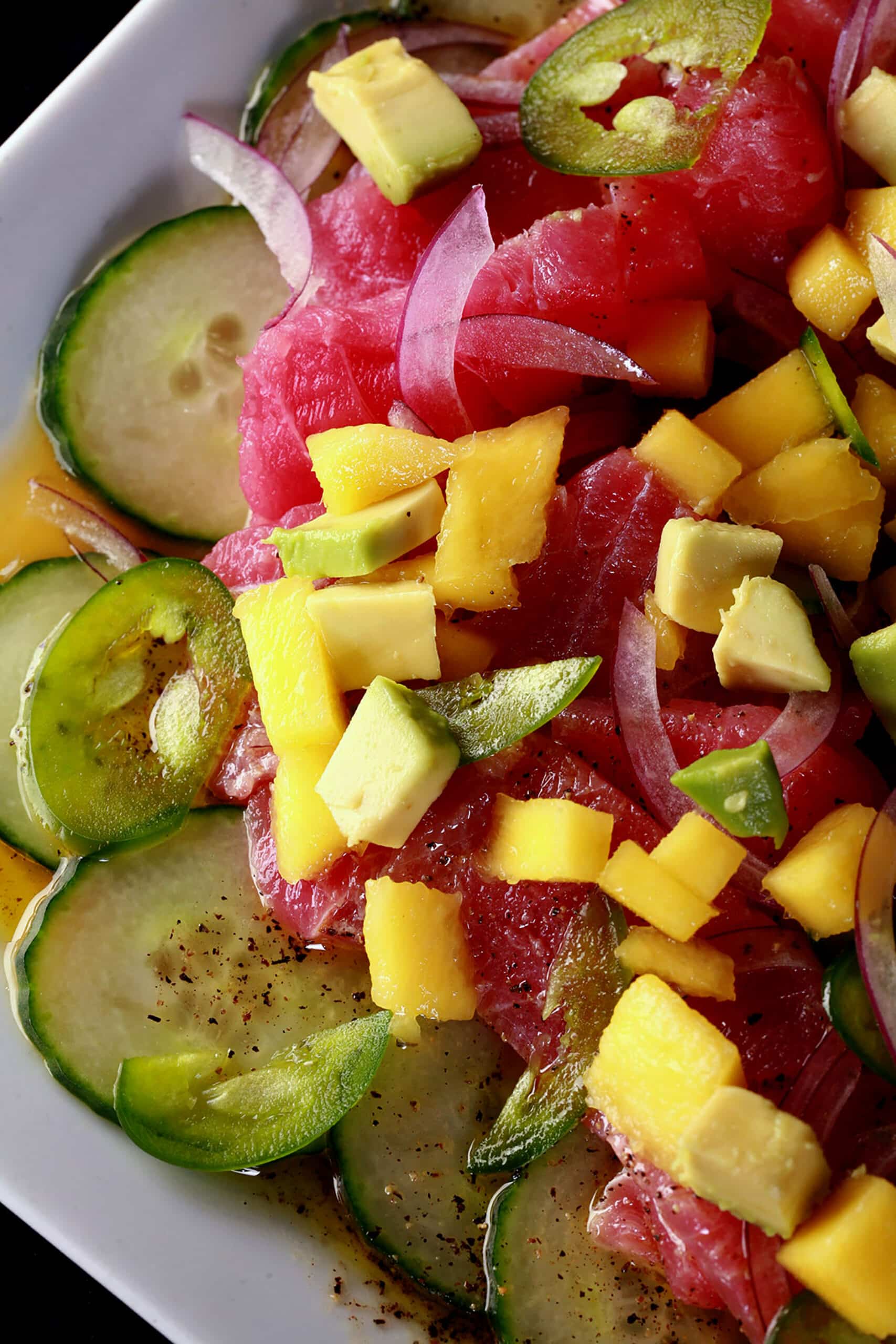 A close up photo of ahi tuna crudo, with mango, avocado, jalapenos, and a citrus vinaigrette, served over cucumber slices.