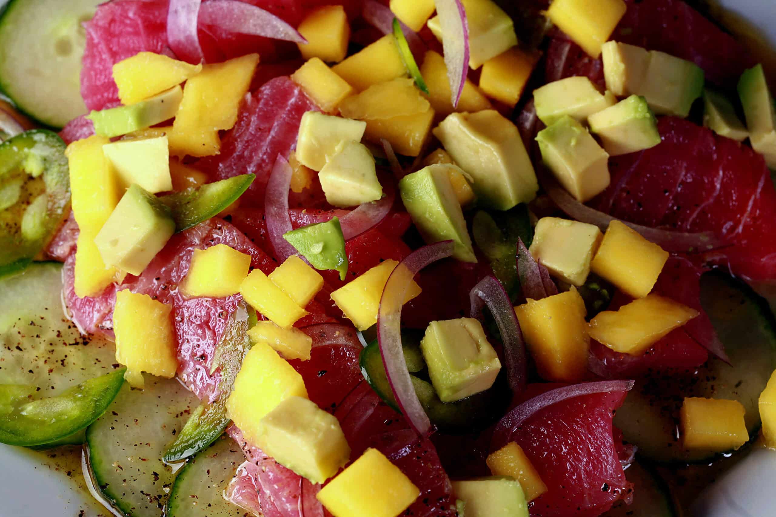 A close up photo of ahi tuna crudo, with mango, avocado, jalapenos, and a citrus vinaigrette, served over cucumber slices.